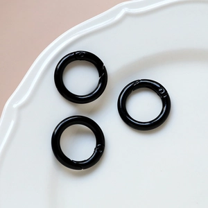 Three glossy black spring O-rings for DIY crafts arranged in a white ceramic dish
