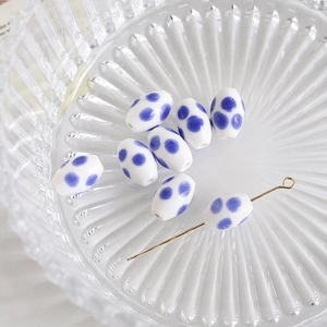 Detail of oval ceramic beads with blue polka dots on white background for DIY jewelry crafts