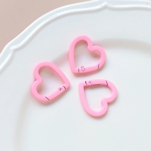 Three pink heart-shaped spring ring clasps for DIY jewelry making on a white plate