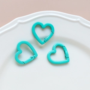 Three mint green heart-shaped spring ring clasps for DIY accessories on a white plate