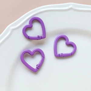 Three purple heart-shaped spring ring clasps on a white ceramic plate for DIY crafts
