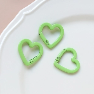 Three bright green heart-shaped lobster clasps for DIY jewelry making on white tray