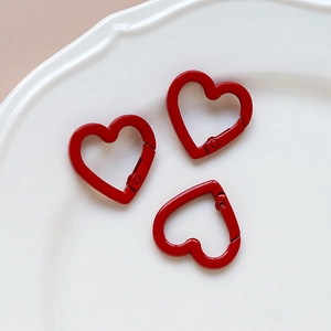 Close-up of three red heart-shaped metal keychains on a white ceramic plate for DIY crafts