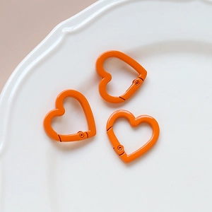 Three orange heart-shaped spring ring clasps for DIY jewelry making on white ceramic tray