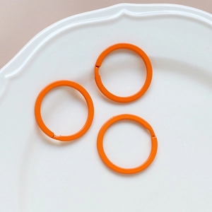 Three vibrant orange split rings on a ceramic tray for DIY jewelry and keychain making