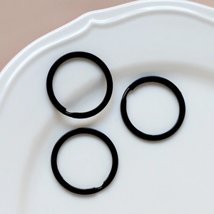 Close-up of three black metal split rings for DIY keychains on a white ceramic plate
