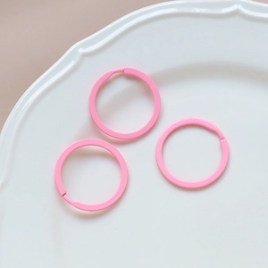 Close-up of three matte pink circular metal key rings for DIY jewelry on a white tray
