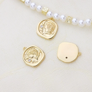 Dettaglio del ciondolo a moneta dorata con rilievo di ritratto e zircone su collana di perle