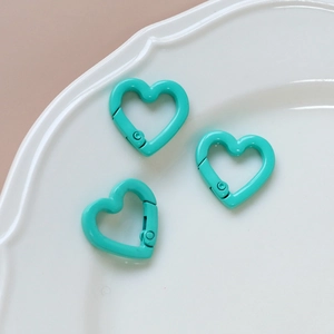 Three mint green heart-shaped spring clasps on a white ceramic plate for DIY jewelry