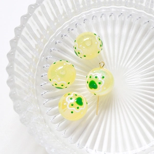 Macro detail of yellow resin beads with green cat paw patterns and gold metal pin