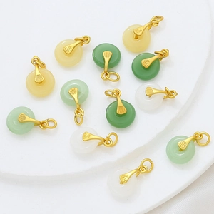 Close-up of small jade ring pendants in white green and yellow with gold-plated clasps