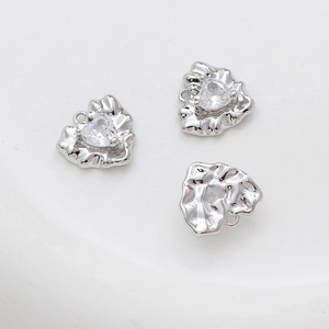 Macro view of silver heart charms with irregular pleated texture and zircon stones