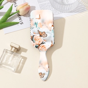 Détail d'une brosse à cheveux à coussin d'air avec motif floral et papillons sur fond beige