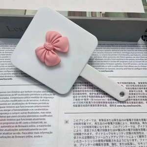 Detail view of a white handheld makeup mirror with a 3D pink bow accent on the back