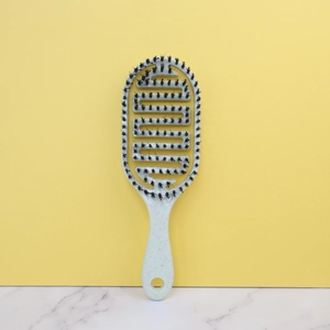 Hollow oval detangling hair brush with massage bristles on marble and yellow background