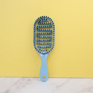Light blue hollowed-out detangling hair brush with S-shaped ventilation slots on yellow backdrop