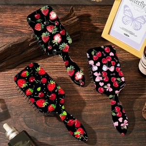 Set di tre spazzole per capelli con stampe di fragole e ciliegie su tavolo in legno