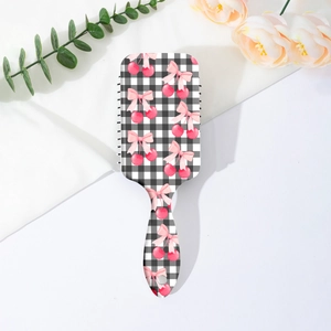 Détail de brosse à cheveux à carreaux avec motif cerise et nœud sur tissu blanc