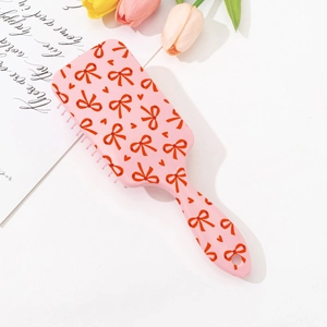 Detail of pink hair brush with cherry bow print and air cushion bristles on white background