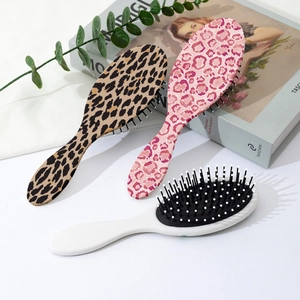 Three leopard print and floral anti-static hairbrushes with ergonomic handles on a desk
