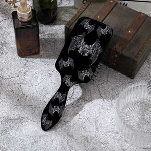 Close-up of gothic black hairbrush featuring grey bat lace prints on a cement surface
