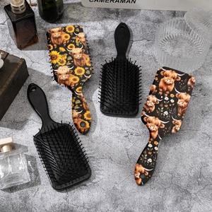 Black cushioned hairbrushes featuring highland cow and sunflower patterns on stone background