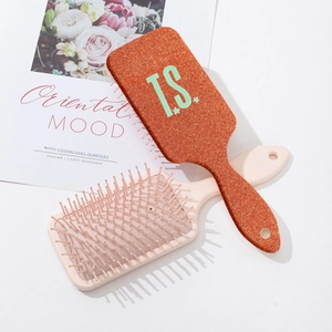 Orange glitter paddle hairbrush with T.S. print and star pattern on white background