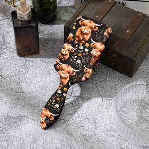 Detail of cushion hairbrush featuring highland cow and daisy print on a stone surface