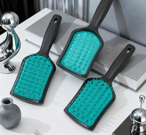 Three vented hair brushes with black handles and green bases on a stylish white desk