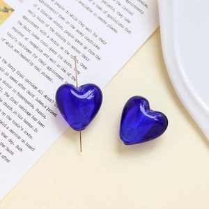 Dettaglio ravvicinato di orecchini a cuore in vetro blu su sfondo di rivista vintage