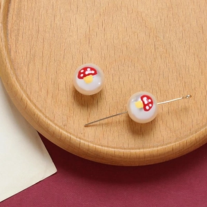 Detailed macro view of translucent DIY beads with red mushroom motifs and silver pins