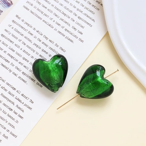 Dettaglio di orecchini a cuore in vetro verde con perni dorati su una rivista