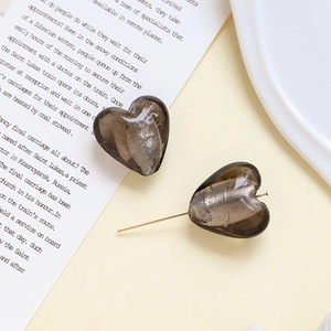 Dettaglio di orecchini a cuore in vetro grigio fumo con lamina d'oro su un libro