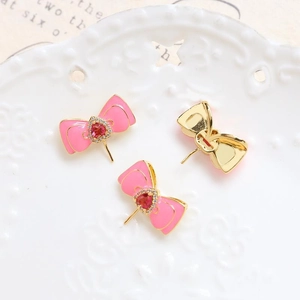 Macro shot of gold-plated pink enamel bow jewelry charms with red heart stone and crystals