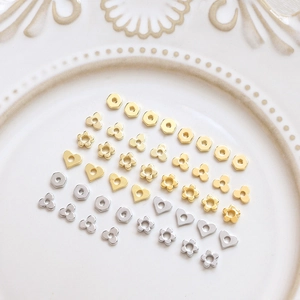 Golden and silver metal geometric spacers in flower and heart shapes on white ceramic