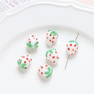 Macro detail of six handmade glass strawberry beads for DIY jewelry making on white ceramic plate