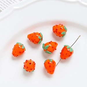 Macro detail of strawberry glass beads for DIY jewelry making on white ceramic plate