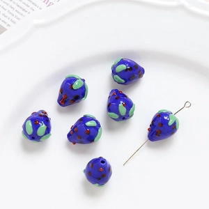 Detailed view of handmade dark blue strawberry glass beads with red dots in a ceramic tray