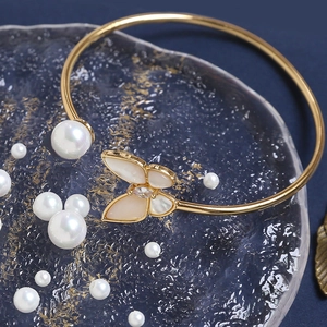 Detailed view of a gold-tone butterfly and pearl bracelet on a glass tray with pearls
