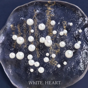 Detailed close-up of high-luster white DIY craft pearls in various sizes on glass