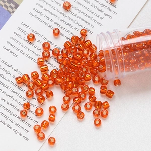 Close-up of 4mm orange glass beads with gold foil spilled from a clear plastic tube