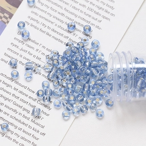 Macro detail of 4mm silver-lined light blue glass beads spilling from clear storage tube