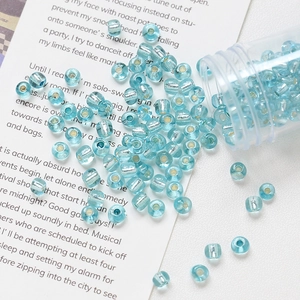 Detail of 4mm light blue silver-lined glass seed beads scattered near a clear storage jar