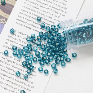 Close-up of 4mm teal glass seed beads with silver inner core pouring from a tube