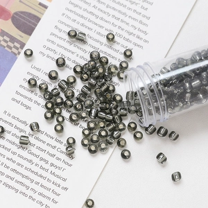 Macro detail of 4mm dark grey glass beads with silver gold foil spilling from a clear tube