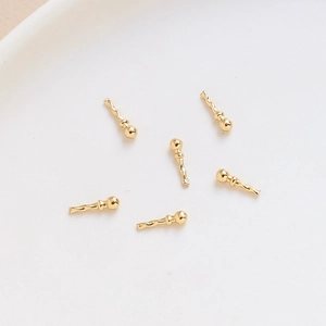 Detail of six gold-plated wavy pin accessories for DIY jewelry making on white ceramic