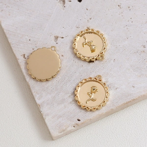 Detailed view of gold plated scalloped edge rose pendant charms on a stone surface