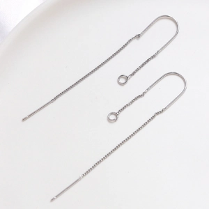 Macro detail of minimalist silver U-shaped chain earrings on white ceramic plate