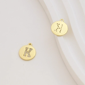 Macro detail of 18k gold plated round letter K charms with cubic zirconia inlay and laser cuts
