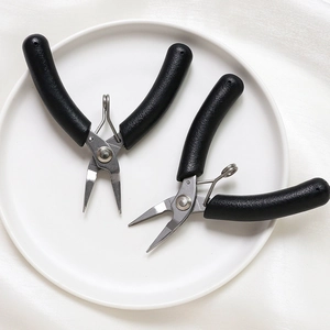 Primer plano de alicates de joyería negros antideslizantes sobre un plato blanco